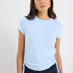 Woman wearing a light blue t-shirt and dark jeans against a plain background