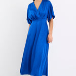 Woman wearing an electric blue satin jacquard midi dress with short kimono sleeves, a wrap-style bodice, and flowing skirt, standing against a white background