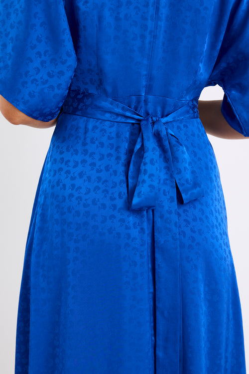 Woman wearing an electric blue satin jacquard midi dress with short kimono sleeves, a wrap-style bodice, and flowing skirt, standing against a white background
