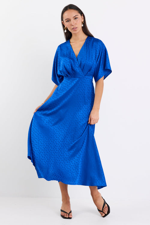 Woman wearing an electric blue satin jacquard midi dress with short kimono sleeves, a wrap-style bodice, and flowing skirt, standing against a white background