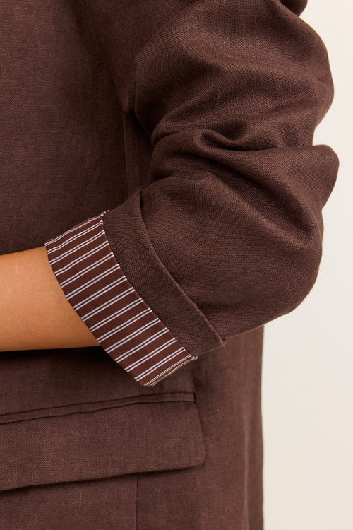 Close-up of a person wearing a brown blazer with a rolled-up sleeve showing a striped lining in brown, beige, and white.