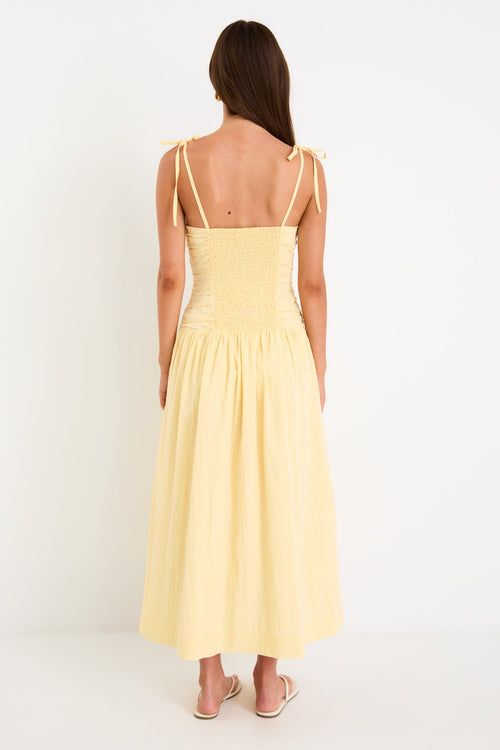 Model wearing a butter-yellow tie-strap maxi dress with a pleated bodice and flowing skirt