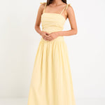 Model wearing a butter-yellow tie-strap maxi dress with a pleated bodice and flowing skirt