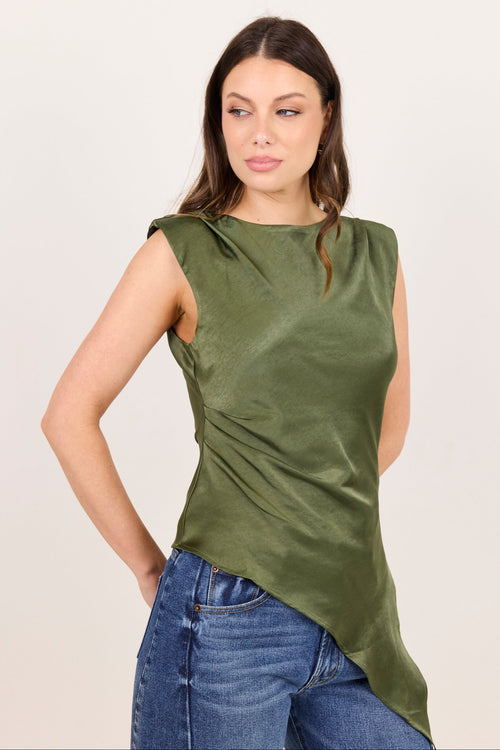 A woman modeling a sleeveless olive green top with a draped, asymmetrical hem and blue jeans, set against a plain light background.