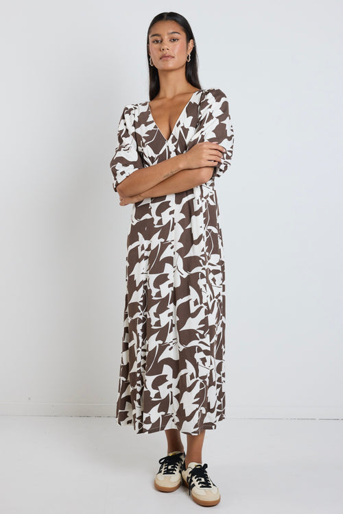 Model wears a brown pattern maxi dress with a v neckline. 