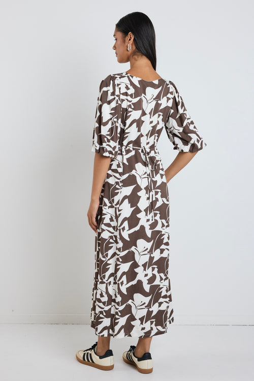 Model wears a brown pattern maxi dress with a v neckline. 