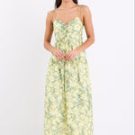 Woman wearing a yellow and green floral print maxi dress with adjustable tie straps, shirred back, and tiered skirt, standing against a white background.