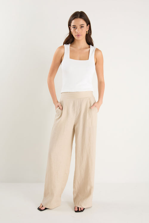 Woman wearing a white tank top and beige wide-leg pants on a white background