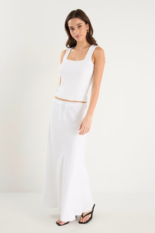 The model wears a white linen maxi skirt with a white tank top