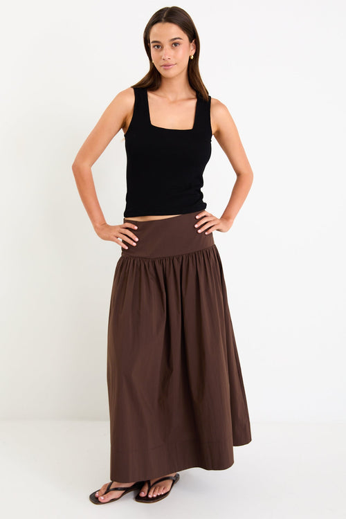 Model wearing a chocolate brown tiered maxi skirt with a flat waistband and shirred back