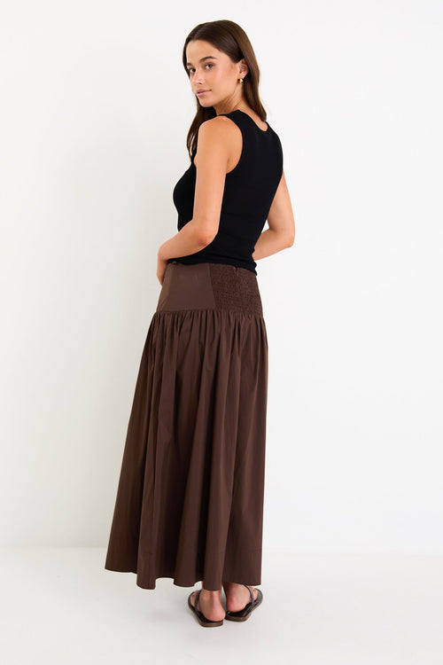 Model wearing a chocolate brown tiered maxi skirt with a flat waistband and shirred back