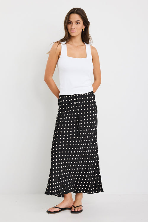 Woman wearing a white tank top and black polka dot skirt on a white background