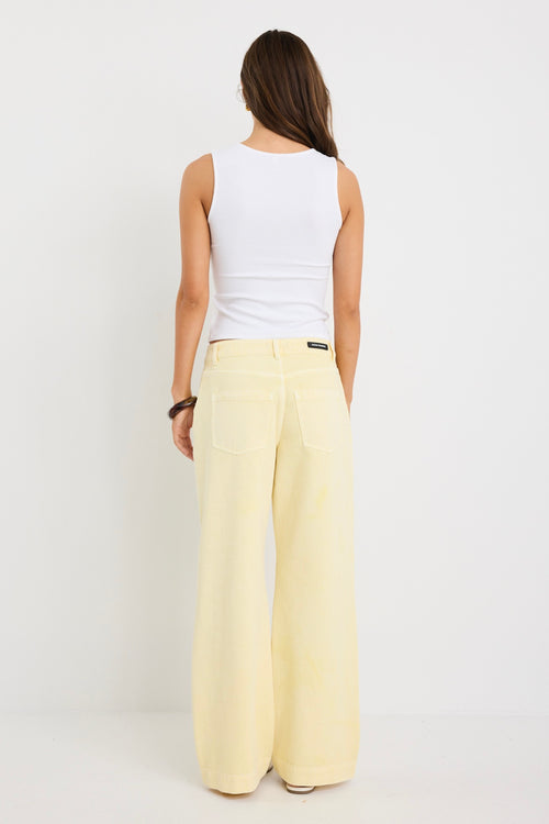 Woman wearing mid-rise wide-leg jeans in a plain butter-yellow wash, styled with a simple white tank and sandals.