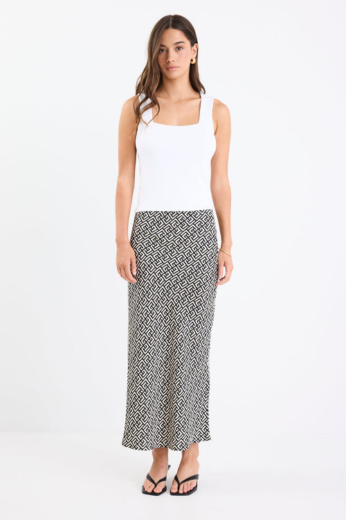 Woman wears a black white geometric print skirt and white tank with black thong heels