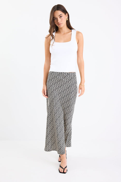 Woman wears a black white geometric print skirt and white tank with black thong heels