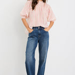 Woman wearing a blush and ivory stripe short sleeve top with a high neck and relaxed fit, styled with blue jeans.