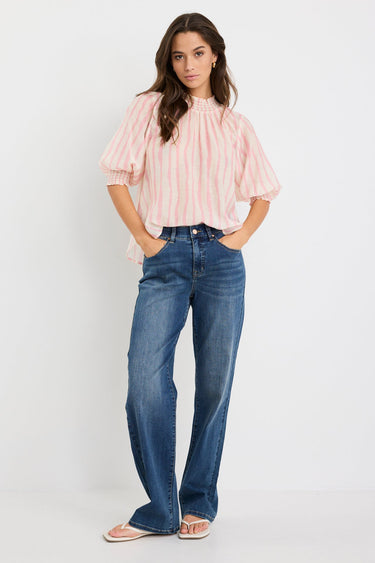 Woman wearing a blush and ivory stripe short sleeve top with a high neck and relaxed fit, styled with blue jeans.