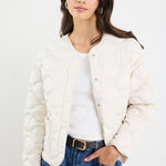 Woman wearing a white puffer jacket, white shirt, and blue jeans on a plain background