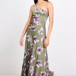 A woman modeling a one-shoulder olive green maxi dress with a purple and white floral print, standing against a plain white studio background.