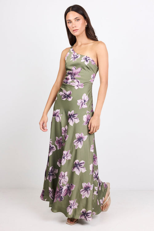 A woman modeling a one-shoulder olive green maxi dress with a purple and white floral print, standing against a plain white studio background.