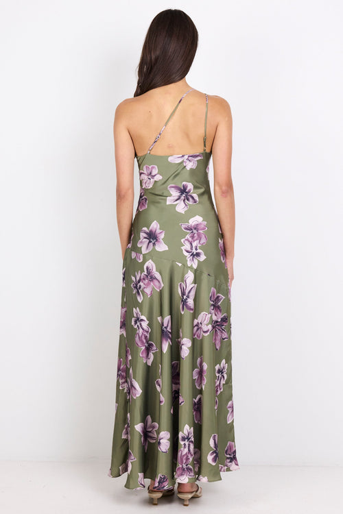 A woman viewed from behind wearing a sleeveless olive green maxi dress with a purple and white floral print, standing against a plain white studio background.