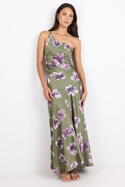 A woman modeling a one-shoulder maxi dress with a green base and a purple floral print, standing against a plain white studio background.