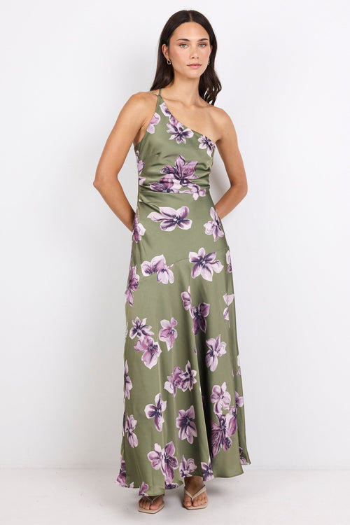 A woman modeling a one-shoulder olive green maxi dress with a purple and white floral print, standing against a plain white studio background.
