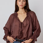 Woman wearing a brown blouse and blue jeans against a plain background