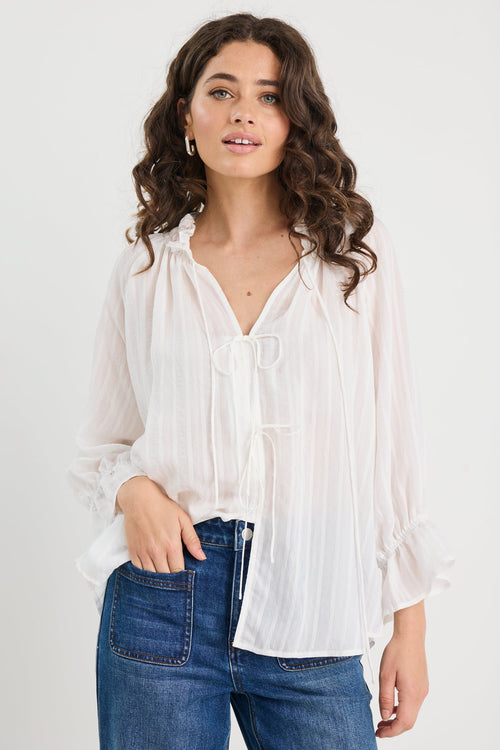 Woman wearing a white blouse and blue jeans against a plain background