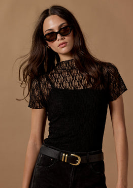Woman wearing a black lace top and high-waisted black pants against a brown background