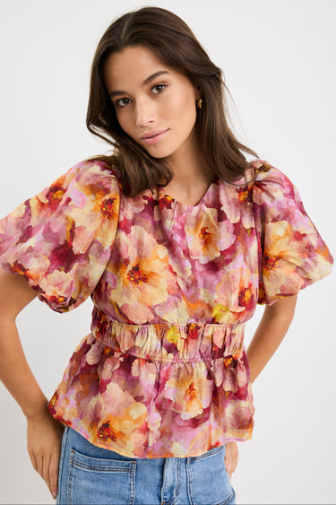 Woman wearing a pink multi floral short sleeve top with bubble sleeves, cinched waist, and crew neckline, styled with blue jeans.