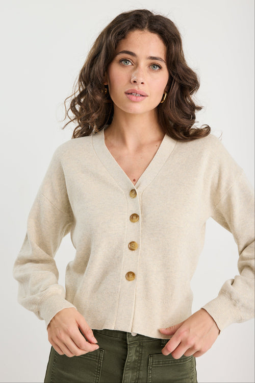 Woman wearing a beige cardigan with gold buttons on a white background