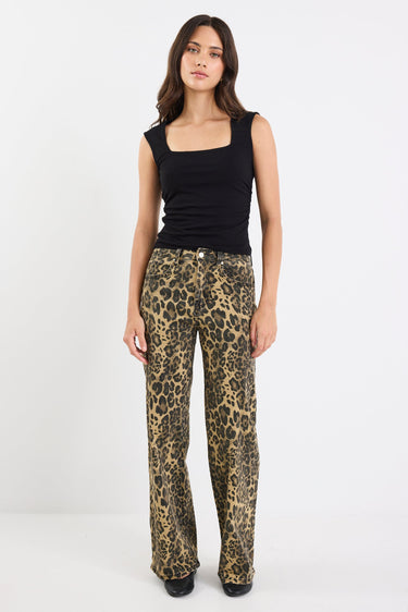 Woman wearing a black sleeveless top and leopard print pants on a white background