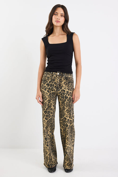 Woman wearing a black sleeveless top and leopard print pants on a white background
