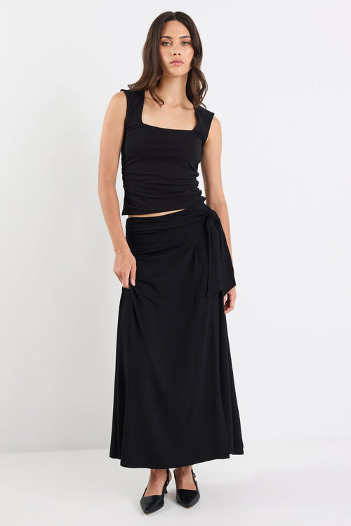 Woman wearing a black sleeveless top and long skirt on a white background