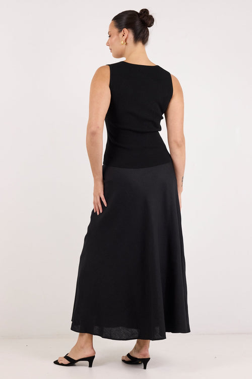 A woman wearing a sleeveless black midi dress with a structured bodice and flowing skirt, shown from the back against a plain white studio background.