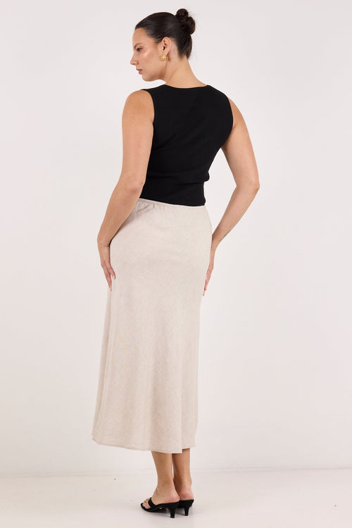 A woman is shown from the back wearing a black sleeveless top and a long, straight, light beige skirt against a plain white studio background.