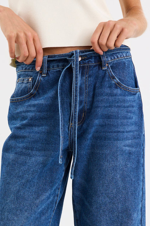 Person wearing blue jeans and white sneakers on a plain background