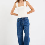 Woman wearing a white tank top and blue jeans on a white background