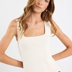 Woman wearing a white tank top and blue jeans on a plain background