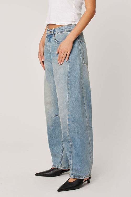 Woman wearing a white top with light wash blue barrel jeans 