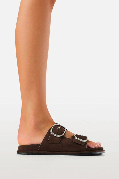 Brown sandal with buckles worn by a person on a light gray background
