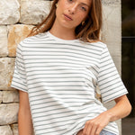 Woman wearing a striped shirt and jeans standing against a stone wall.