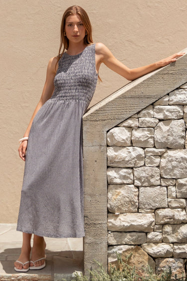 Woman in a gray dress standing against a beige wall with stone architecture.
