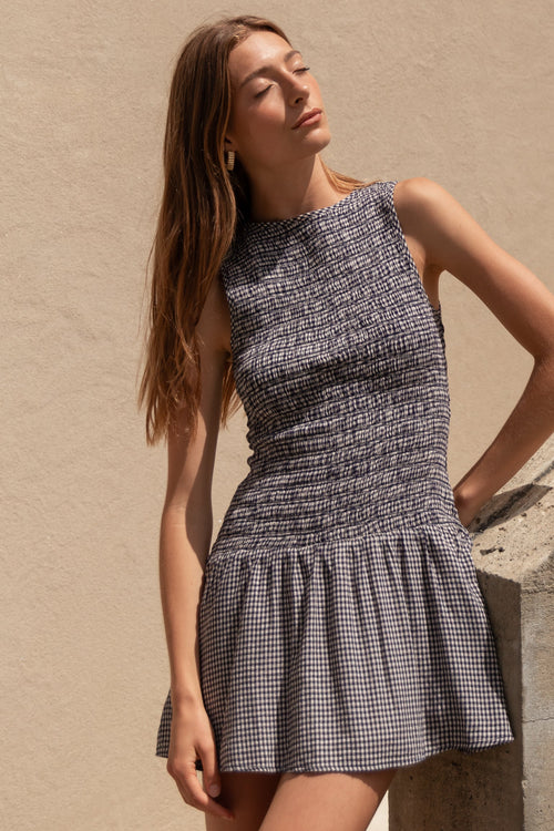 Woman in a checkered dress standing against a beige wall.