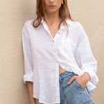 Woman in a white shirt and denim shorts standing on a staircase with a neutral wall background