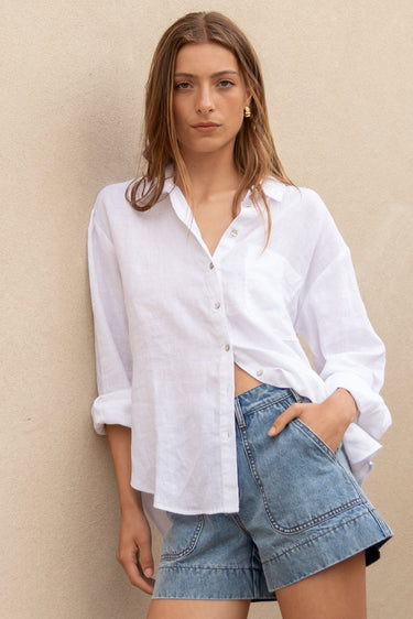 Woman in a white shirt and denim shorts standing on a staircase with a neutral wall background