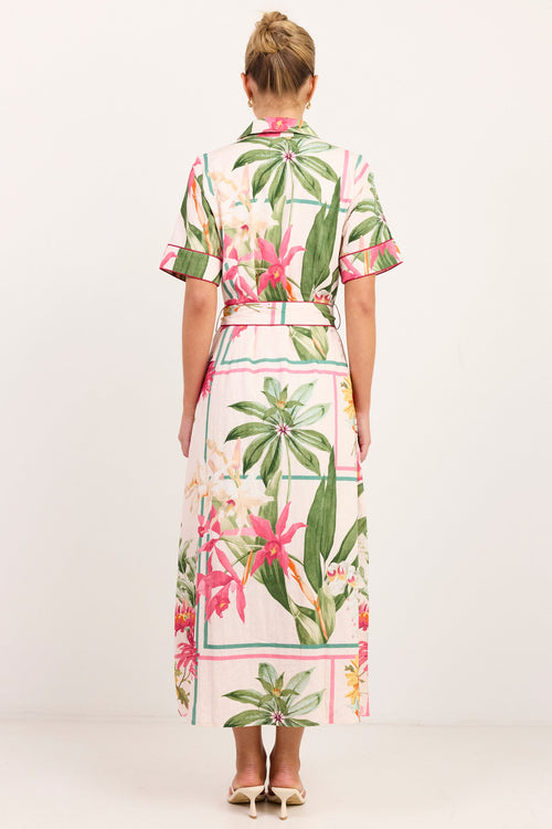 A woman viewed from behind wearing a short-sleeve midi dress with a tropical floral print and a thin matching waist belt, set against a plain white studio background.
