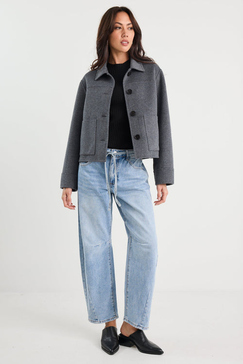 Person wearing a gray jacket, black shirt, light blue jeans, and black shoes on a white background
