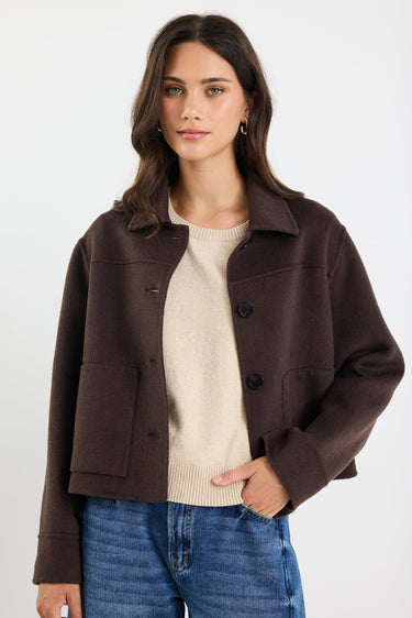 Woman wearing a brown jacket over a beige sweater and blue jeans on a white background